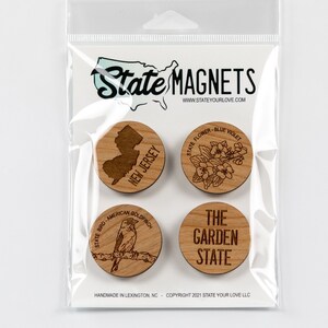 May include: Set of four wooden magnets featuring New Jersey state symbols. The magnets include the state outline, the state bird, the state flower, and the nickname "The Garden State".