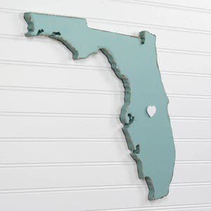 May include: A teal blue wooden cutout of the state of Florida with a white heart pin in the center.