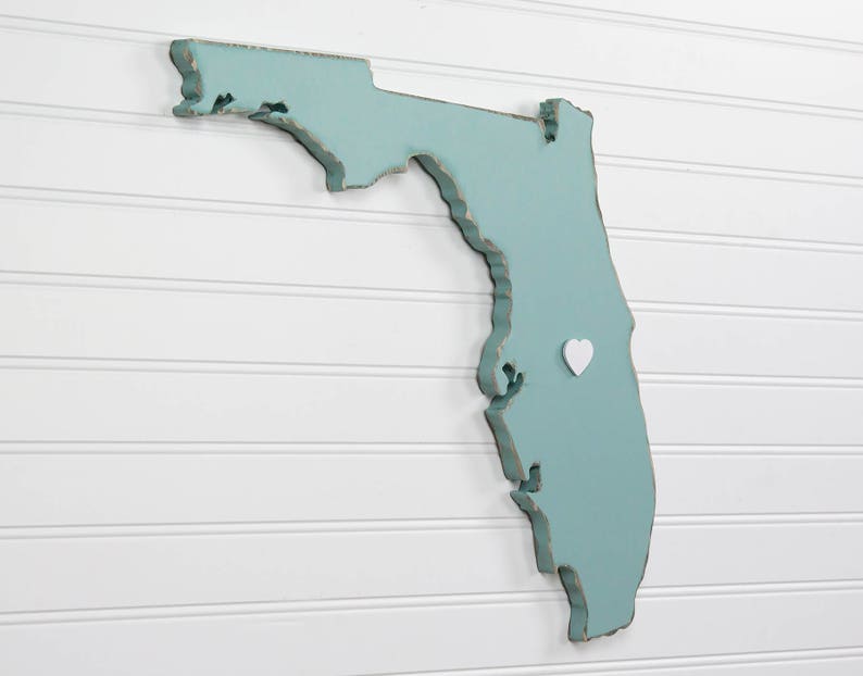 May include: A teal blue wooden cutout of the state of Florida with a white heart pin in the center.