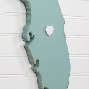 May include: A teal blue wooden outline of the state of Florida with a white heart in the center.