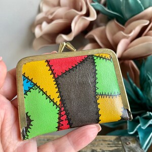 Puede incluir: Una peque&ntilde;a cartera de monedas colorida con un dise&ntilde;o de patchwork. La cartera est&aacute; hecha de cuero y tiene un cierre de lat&oacute;n. Los colores del patchwork son rojo, amarillo, verde, azul y negro.