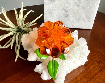 Op de afbeelding: Oranje glazen bloem met groene bladeren op een witte koraalachtige basis.