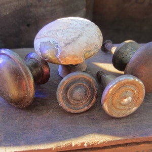 May include: Five antique brass cabinet knobs with varying designs. Some have a circular design, while others have a more rounded shape. The knobs are in various shades of brass, with some showing signs of wear and patina.