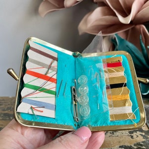 Puede incluir: Un peque&ntilde;o kit de costura de metal dorado con un forro turquesa. El kit est&aacute; abierto y contiene carretes de hilo, agujas y botones. El texto "MADE IN" es visible en el lado derecho del kit.