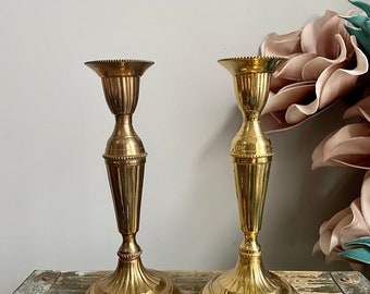 Puede incluir: Dos candelabros de metal dorado con un diseño acanalado. Los candelabros tienen una base redonda y un cuerpo alto y delgado.
