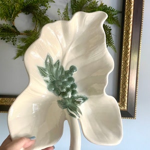 May include: A white ceramic leaf-shaped serving dish with a green grape cluster and leaves design.