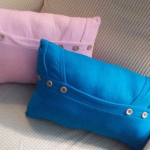 May include: Two decorative pillows with button accents. The pillow on the bottom is blue and the pillow on top is pink.