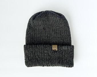 May include: A dark gray knitted beanie with a brown leather patch featuring a mountain logo.