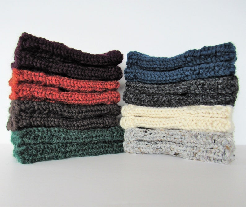 Puede incluir: Una pila de ocho diademas de punto en varios colores, incluyendo burdeos, naranja, gris oscuro, verde, azul marino, gris, crema y gris con motas blancas.