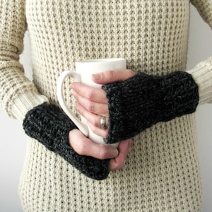 Puede incluir: Un par de guantes sin dedos grises con un patr&oacute;n de punto texturizado. Los guantes est&aacute;n siendo usados por una persona que sostiene una taza blanca.