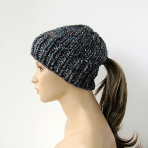 May include: A gray, blue, and purple knit beanie with a ponytail hole. The beanie is made of a soft, chunky yarn and has a simple, classic design.