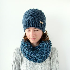 May include: A blue knitted beanie and matching infinity scarf. The beanie has a textured knit pattern and a small brown label.