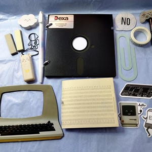 May include: A selection of retro stationery and accessories, including a black floppy disk, a vintage computer, stickers, a pen, and a pencil. The items are arranged on a light blue surface.