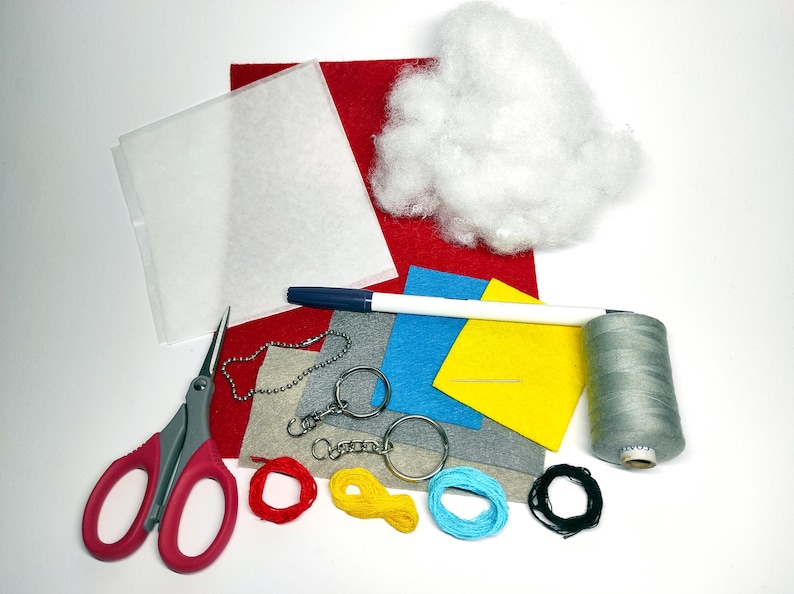 K&ouml;nnte beinhalten: Ein Bastelset zum Herstellen eines Schl&uuml;sselanh&auml;ngers. Das Set enth&auml;lt Filz in Rot, Blau, Gelb und Grau, einen wei&szlig;en Stift, eine Nadel, Garn, eine Schere, einen Schl&uuml;sselring und F&uuml;llmaterial.