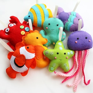 May include: A set of nine felt sea creature ornaments, including a red crab, an orange and white clownfish, a yellow seahorse, a green starfish, a turquoise octopus, a purple jellyfish, and a blue and green fish.