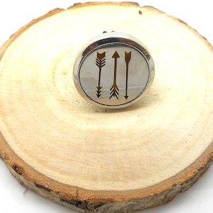 Könnte beinhalten: Runder Diffusor-Anhänger aus Silber mit einem Design aus drei nach oben zeigenden Pfeilen. Die Pfeile sind in Silber umrandet und mit einer gelben Farbe gefüllt.