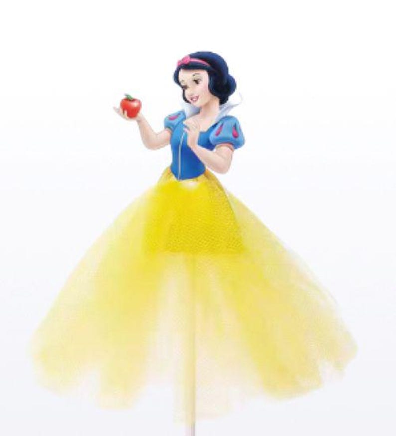 May include: A Snow White figurine holding a red apple. The figure wears a blue top with puffy sleeves, a yellow skirt, and a red headband. The figurine is a cake topper.