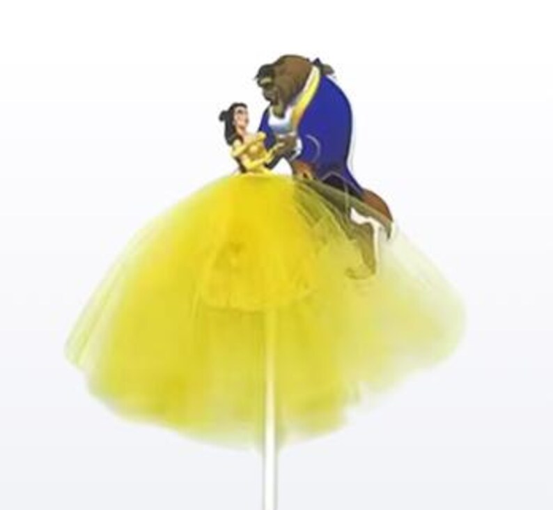 May include: A yellow tulle skirt with a cartoon cutout of Belle and the Beast dancing. The figures are on a stick, likely a cake topper. The skirt is a bright, sunny yellow.