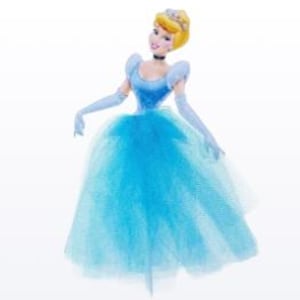 May include: A Cinderella figurine in a light blue ball gown with a tulle skirt, matching gloves, and a choker. The doll has blonde hair styled in a bun and a tiara. The figurine is posed with arms outstretched.