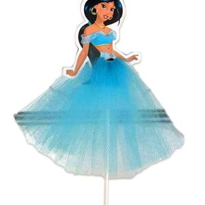 May include: A princess-themed cake topper featuring a cartoon illustration of a woman in a blue outfit with a tulle skirt. The figure has dark hair, gold jewelry, and is mounted on a white stick.