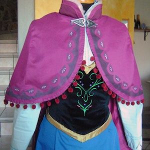 May include: A purple and blue dress with a black bodice and a white fur collar. The dress has a gold trim and a silver snowflake brooch. The dress is a costume for a popular animated character.