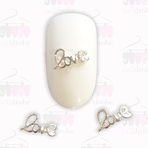 May include: Three silver nail charms shaped like the word "Love" in a cursive font.