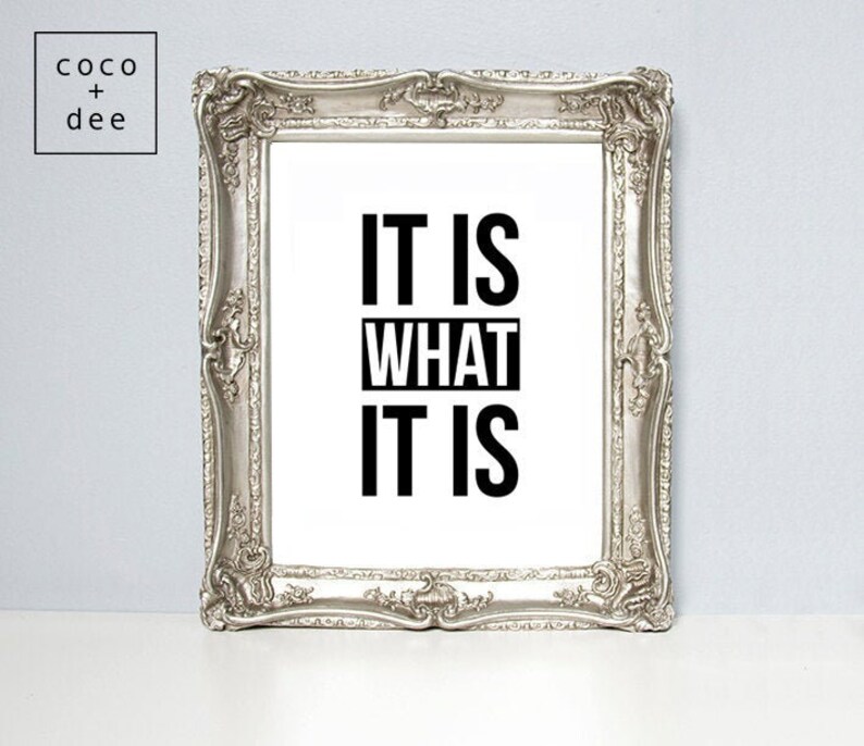 May include: Silver framed wall art with the text "IT IS WHAT IT IS" in bold black letters on a white background. The frame has ornate detailing and a rectangular shape. The upper left corner has the text "coco + dee".