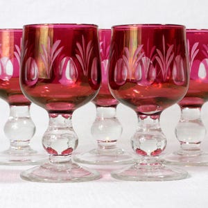 May include: Set of six ruby red stemmed wine glasses with a clear glass base and etched white floral designs.