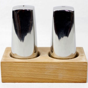 May include: Two silver salt and pepper shakers on a wooden base. The shakers are cylindrical and have a shiny finish.