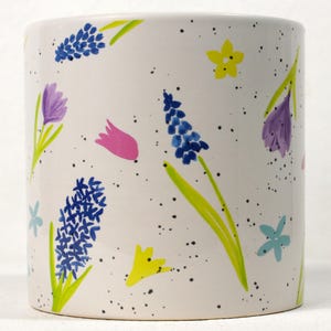 May include: White ceramic planter with a floral pattern. The planter features blue, pink, yellow, and purple flowers on a white background with black speckles.