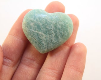 Peut inclure: Un cristal d'aventurine vert en forme de cœur. Le cristal a une surface lisse et polie et une couleur vert clair avec des stries blanches.