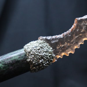 May include: A decorative knife with a translucent, serrated blade made of a light brown material. The handle is made of a dark green and black stone with a silver-coloured metal cap.