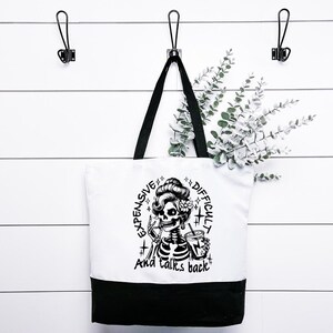 Puede incluir: Bolsa de tela negra y blanca con un esqueleto sosteniendo una bebida y el texto "Expensive + Difficult + And talks back".