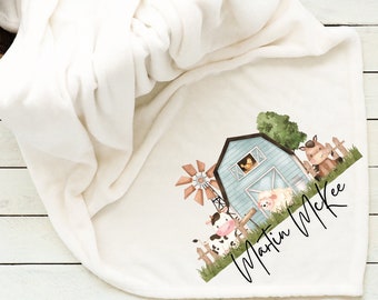 May include: A white fleece baby blanket with a farm scene printed on it. The scene includes a blue barn, a windmill, a cow, a sheep, a horse, and a chick. The text "Martin McKee" is printed below the scene.