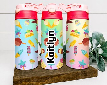 Peut inclure: Trois gourdes cylindriques avec des couvercles roses et un motif coloré de cornets de glace, de sucettes glacées et d'étoiles. La bouteille centrale porte le nom Kaitlyn imprimé verticalement en lettres noires sur un fond dégradé clair.