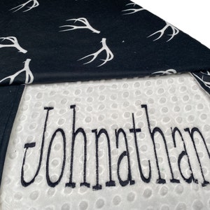 May include: A white minky baby blanket with a black and white antler print on one side. The other side is white with the name "Jonathan" embroidered in black.