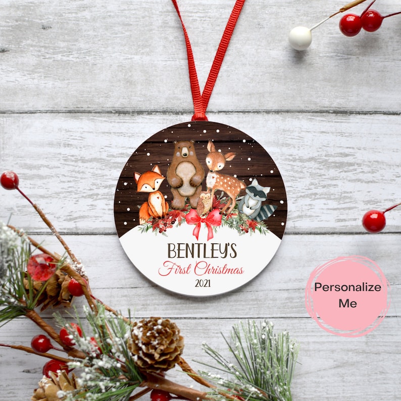 Puede incluir: Un adorno navide&ntilde;o redondo y blanco con un fondo de madera marr&oacute;n que presenta un zorro, un oso, un ciervo, un b&uacute;ho y un mapache. El adorno tiene el texto "Bentley's First Christmas 2021" impreso en &eacute;l.