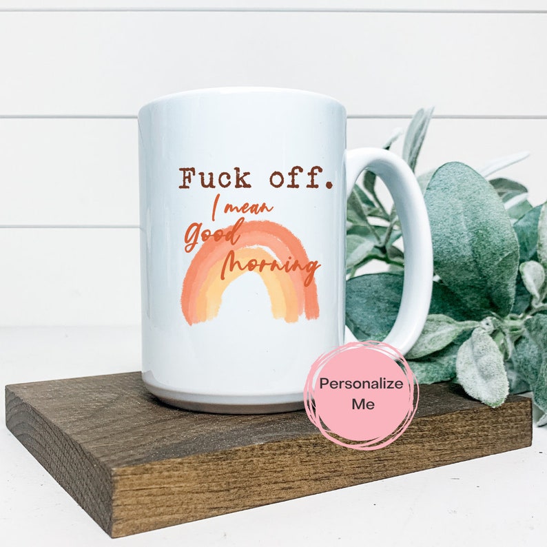 Pode incluir: Caneca de caf&eacute; de cer&acirc;mica branca com um design de arco-&iacute;ris e o texto "Fuck off. I mean Good Morning".