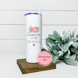 May include: White stainless steel tumbler with a blue lid and a straw. It features a floral design and the text "Ringmaster of the Shitshow" with a heart.