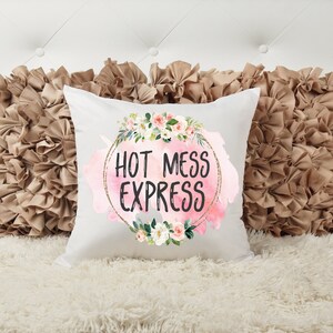 May include: White throw pillow with a pink watercolor background and gold glitter circle. The circle has the text "HOT MESS EXPRESS" in black lettering and is surrounded by a floral wreath.