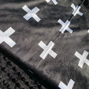 May include: Black and white throw blanket with a repeating pattern of white crosses. The blanket is made of a soft, fuzzy material.