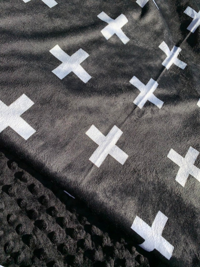 May include: Black and white throw blanket with a repeating pattern of white crosses. The blanket is made of a soft, fuzzy material.