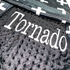 May include: Black and white baby blanket with a white cross pattern on one side and a black minky fabric with the name "Tornado" embroidered in white on the other side.