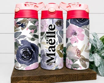Peut inclure: Trois gourdes avec des couvercles roses et un motif floral composé de roses aquarelles bleu marine et violet clair avec des feuilles vertes. La bouteille centrale affiche le prénom Maëlle en texte vertical noir sur le motif floral.