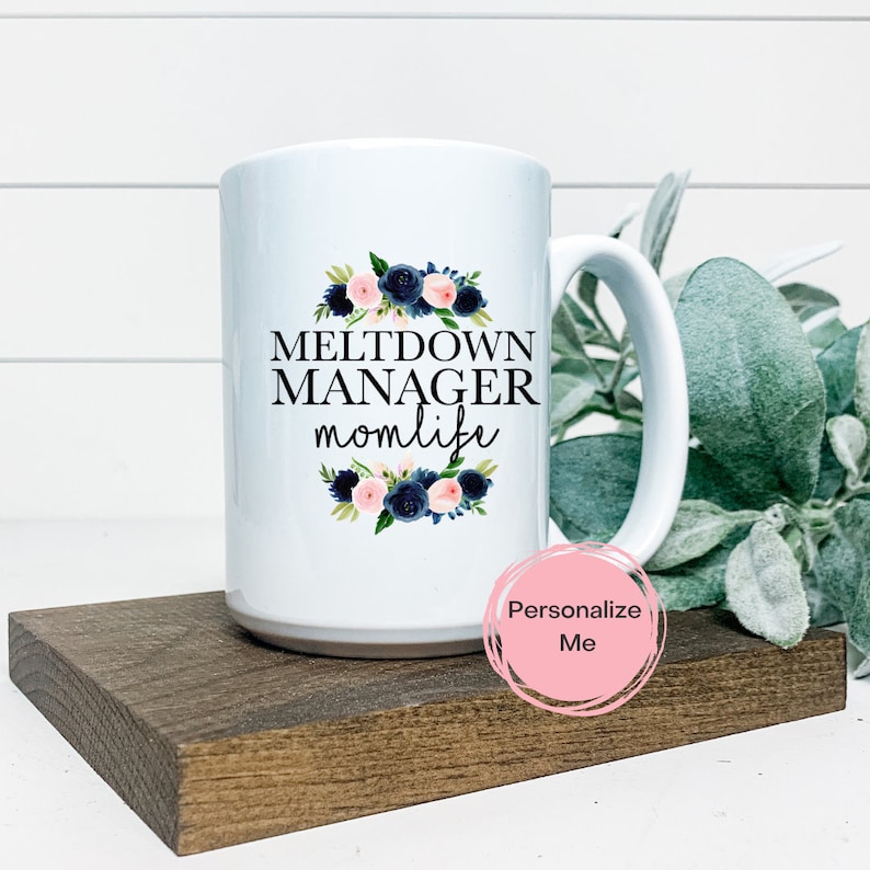 K&ouml;nnte beinhalten: Eine wei&szlig;e Keramik-Kaffeetasse mit einem schwarzen Blumendesign und dem Text "Meltdown Manager momlife".