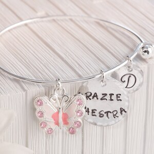 Può includere: Braccialetto in argento con un ciondolo a forma di farfalla rosa, un ciondolo con il testo "Grazie Orchestra" e un ciondolo con la lettera "D".