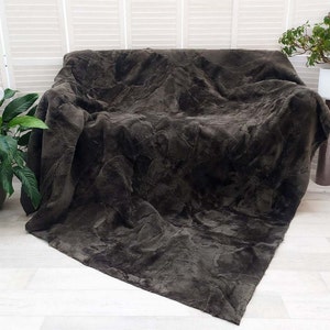 May include: A dark brown sheepskin throw blanket with a soft, fluffy texture. The blanket is draped over a couch and has a natural, rustic look.