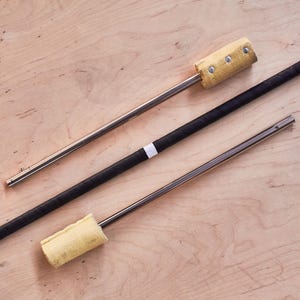 May include: Three fire spinning props on a light wood surface. Two are silver metal rods with a yellow fabric end, and one is a black wrapped rod with a white band. The props are designed for fire performance and flow arts.
