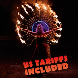 May include: A large circular metal fire prop with multiple flames burning along its outer edge, positioned behind a person wearing a dark dress. The text US TARIFFS INCLUDED is displayed in bold orange letters at the bottom of the image.