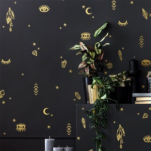 May include: A black wall with gold decorative decals featuring stars, moons, eyes, crystals, and feathers. The wall is decorated with two potted plants and a framed picture.